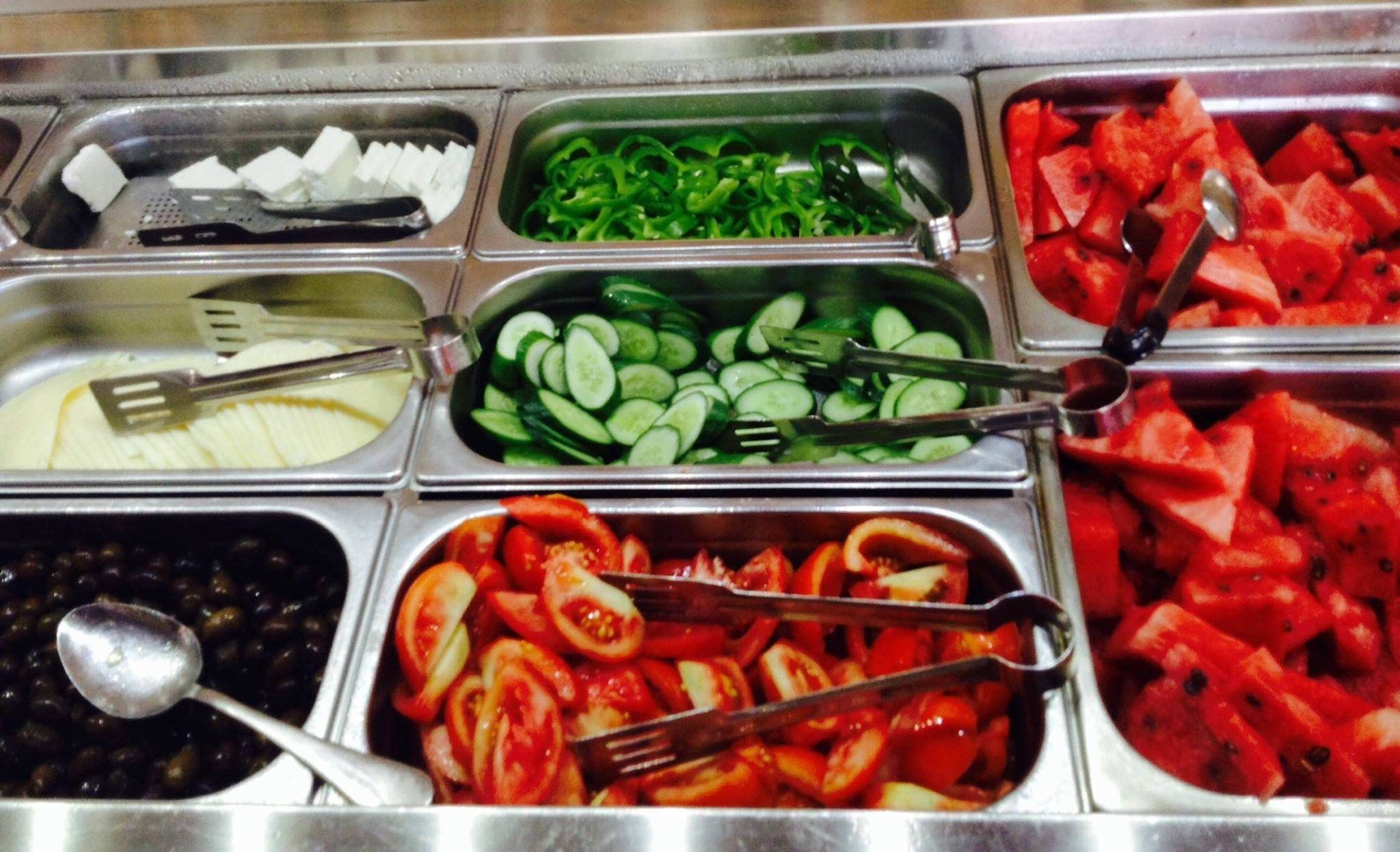 A buffet with various food items including sliced cucumbers, tomatoes, watermelon, and cheese.