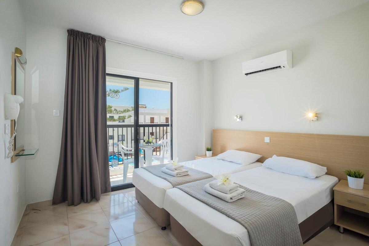 Habitación de hotel con dos camas, un balcón con vistas y aire acondicionado.