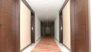 Un couloir d’hôtel avec des portes en bois, une moquette rouge et des luminaires encastrés.