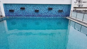 Une piscine dont le mur est recouvert d’une mosaïque bleue en carreaux et qui est bordée de rampes en métal.