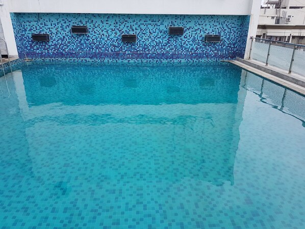 A swimming pool with a tiled blue mosaic wall and metal railings.