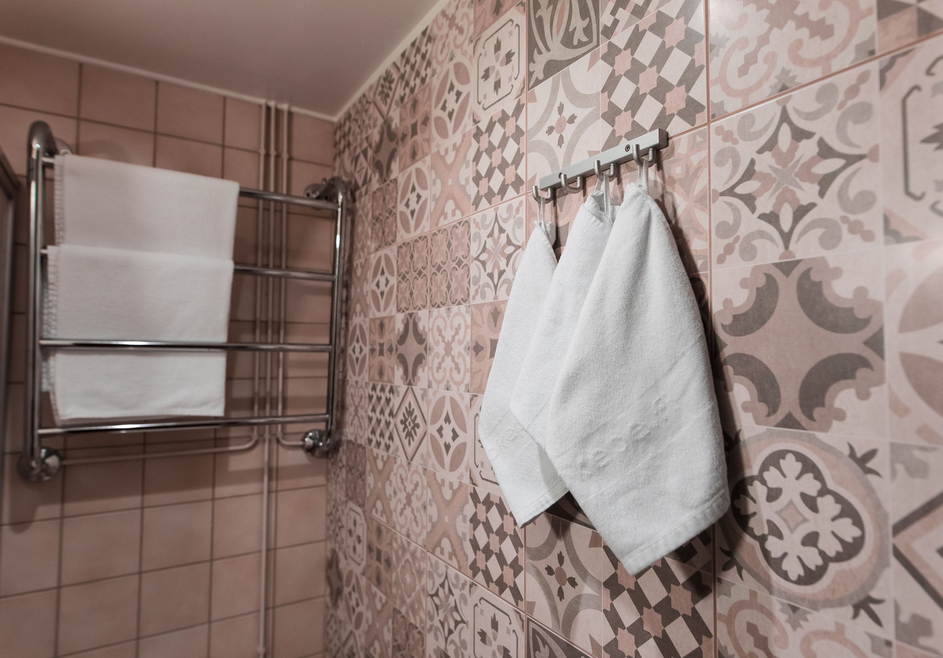 A bathroom with patterned tiles, a towel rack, and a towel hanging on the wall.