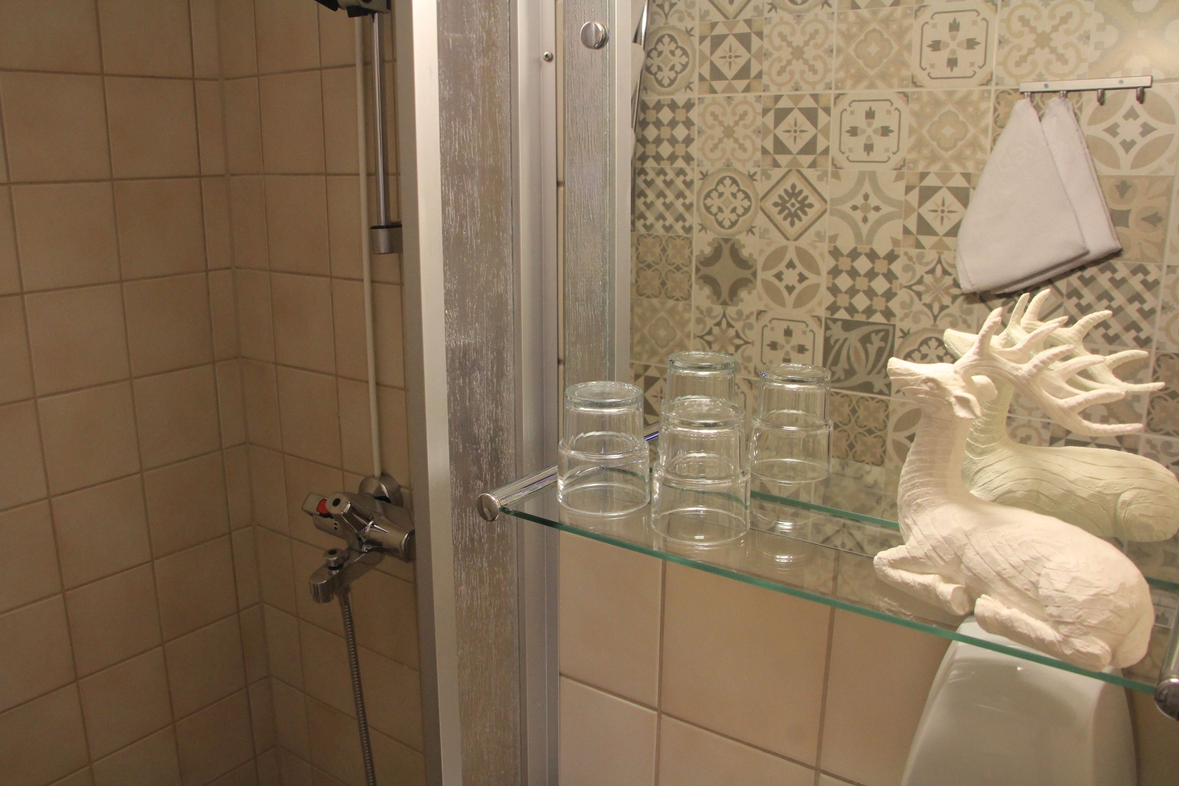 Un baño con ducha, repisas de vidrio y azulejos con diseño.