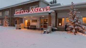 Um hotel com fachada coberta de neve e letreiros iluminados.
