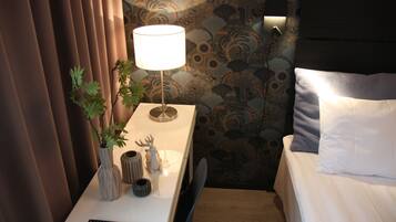 A neatly made bed with white linens, a bedside lamp, a remote control, and a small plant on a bedside table.