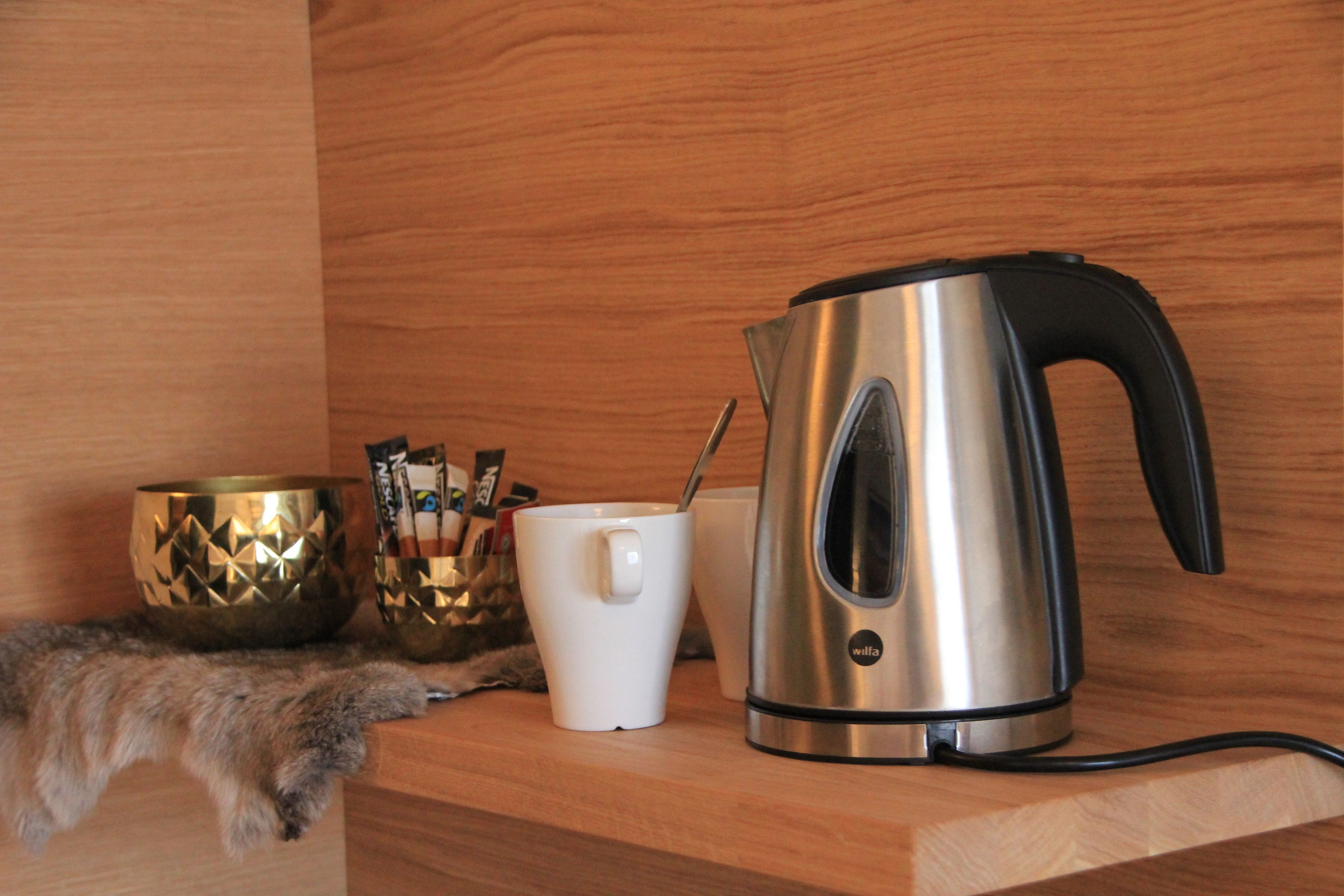A stainless steel kettle, a white mug, and a decorative bowl on a wooden shelf.
