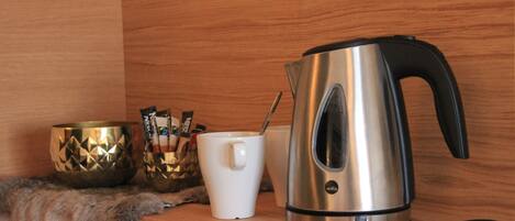 A stainless steel kettle, a white mug, and a decorative bowl on a wooden shelf.