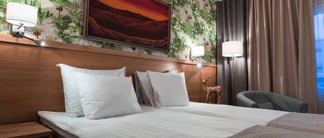 A hotel room with a large bed, two bedside tables, a nightstand, a chair, a wall-mounted lamp, and a painting of a sunset.
