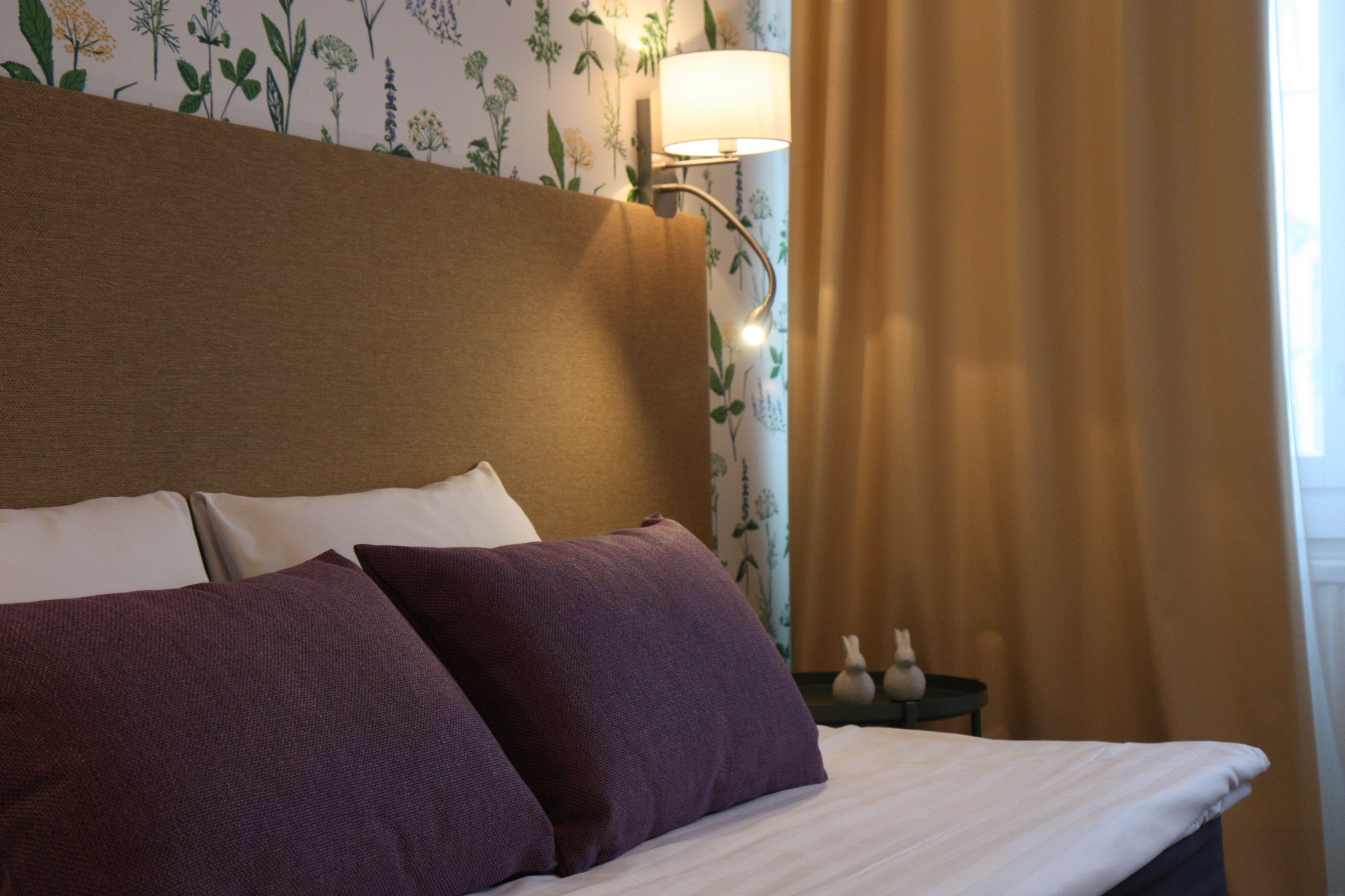 A neatly made bed with two pillows, a headboard, and a wall with floral wallpaper.