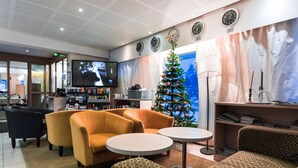 Una hall con posti a sedere, un albero di Natale, un televisore e orologi alle pareti.