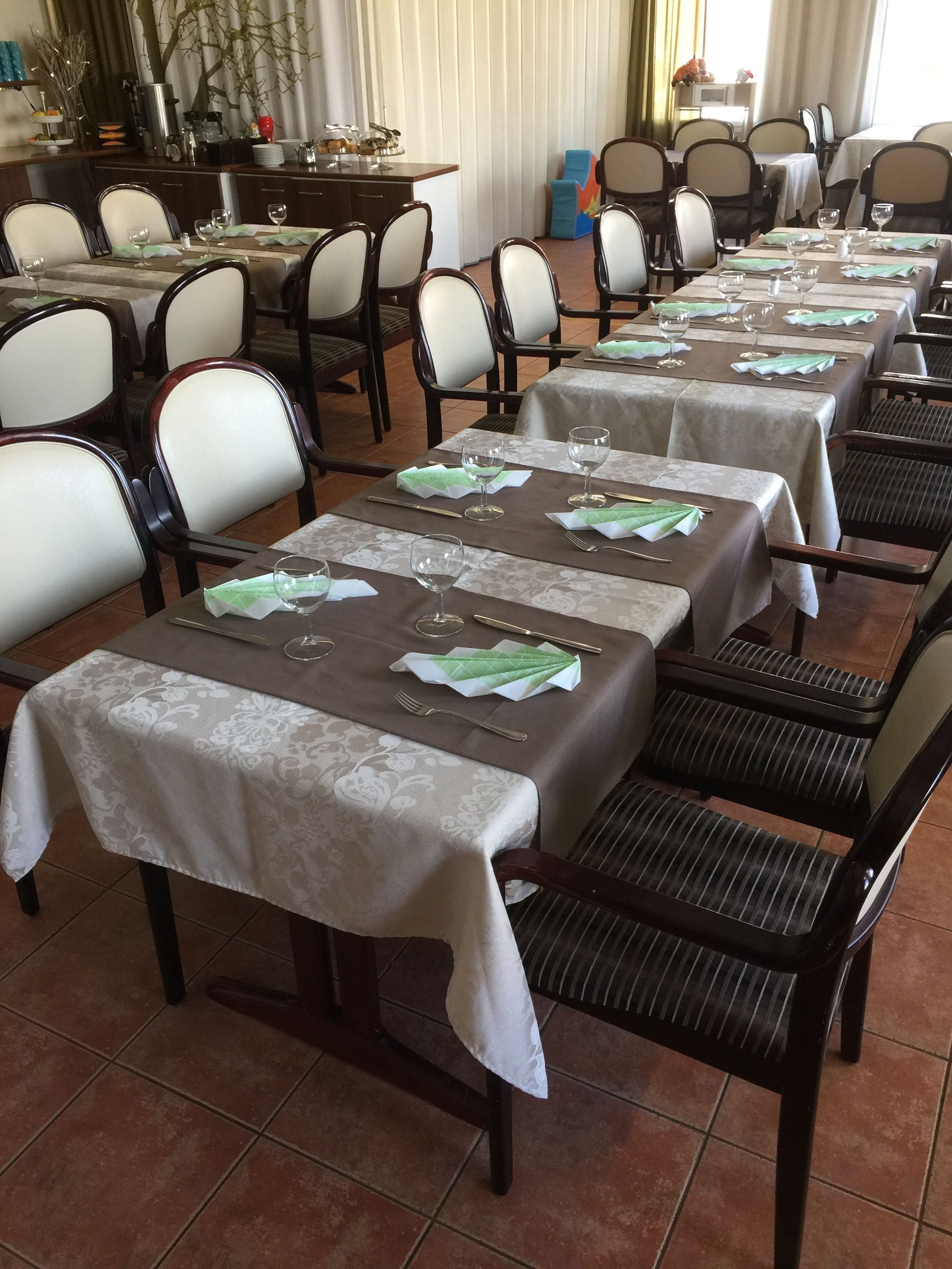 Un espace repas avec plusieurs tables dressées pour le service, chacune étant agrémentée d’une nappe, de chaises et de couverts.