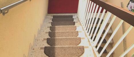 Una escalera con alfombra roja, barandilla blanca y suelo texturizado.