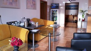 Un hall d’hôtel avec des canapés à rayures, un coin café, un réfrigérateur rempli de boissons et un téléviseur diffusant un programme d’information.