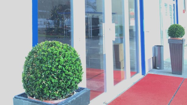 L’entrée d’un hôtel, avec un tapis rouge, de grandes fenêtres en verre et une enseigne indiquant « New Fair ».