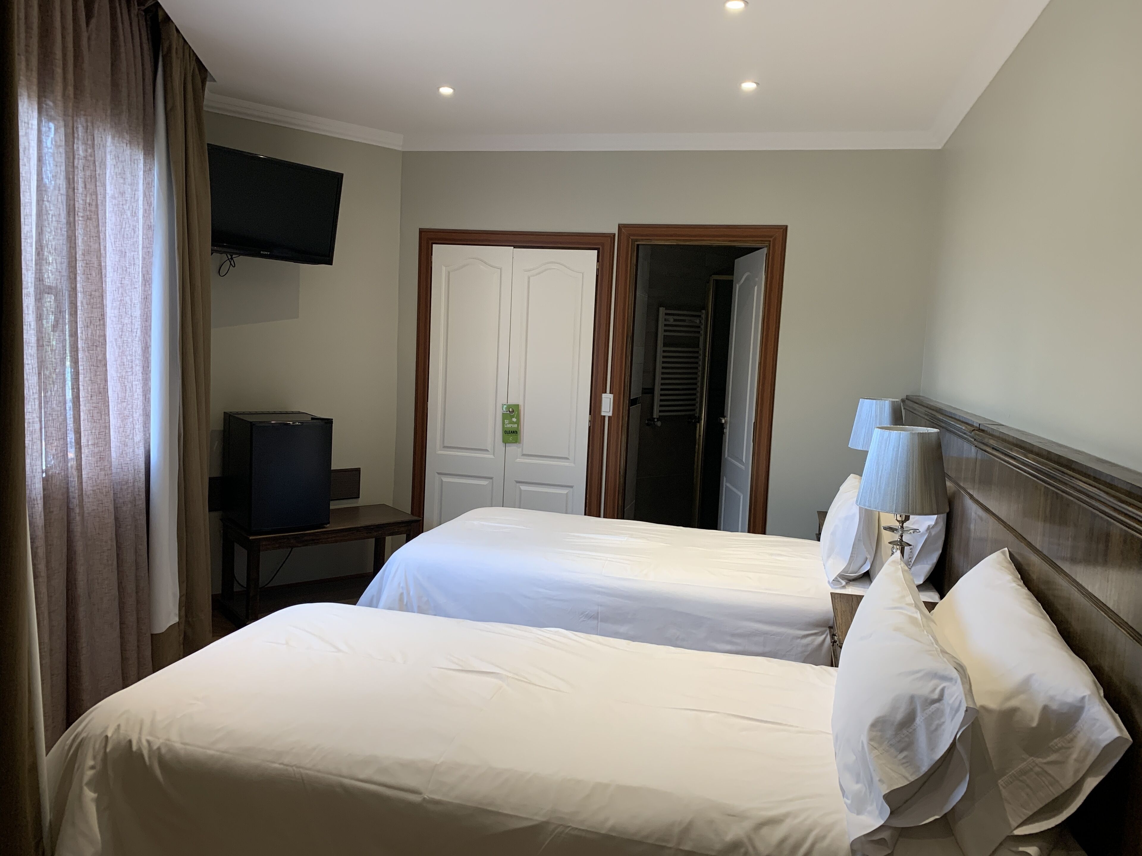 A hotel room with two beds, a television, a desk, and a door leading to a bathroom.