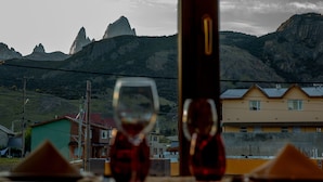 Una mesa con dos copas de vino tinto, una botella y un servilleta triangular, con montañas y edificios como fondo.