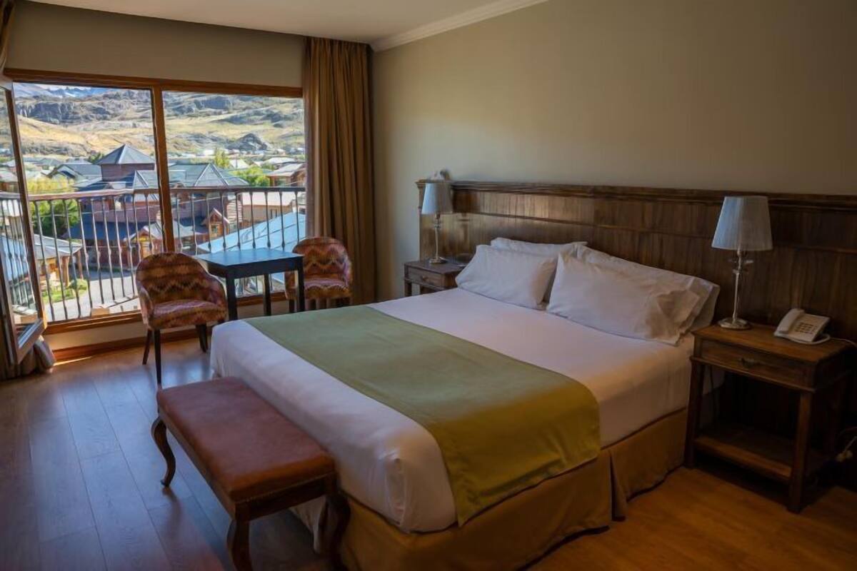 Une chambre d’hôtel avec un grand lit, une banquette, une chaise, une table de chevet avec un téléphone et une vue sur les montagnes par la fenêtre.