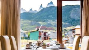 Una mesa de comedor dispuesta con platos, vasos y una planta en maceta, con vista a una montaña a través de una ventana.