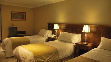 A hotel room with two single beds, each with a bedside table and lamp, a wooden headboard, and a framed artwork on the wall.