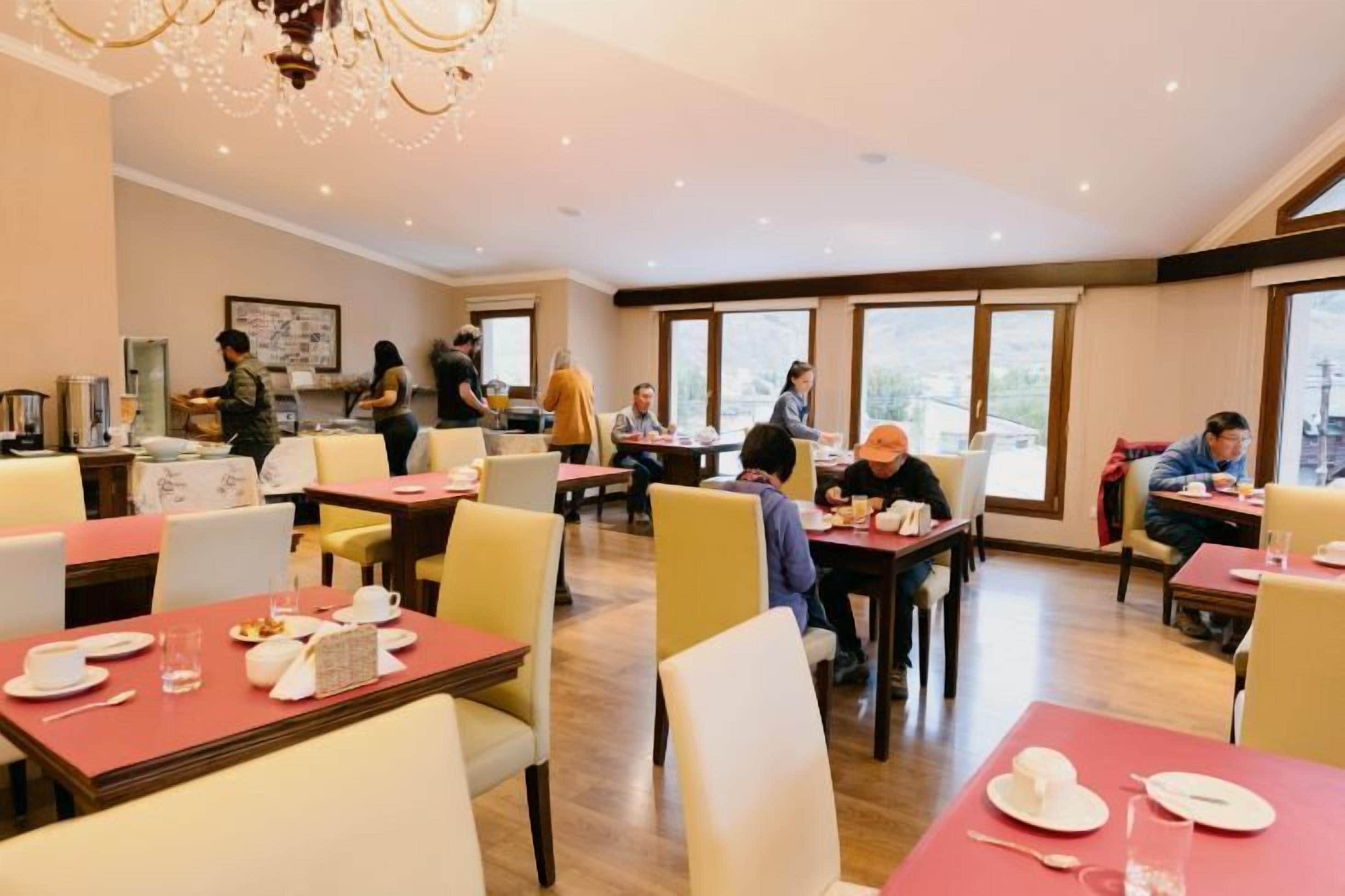 Un espace repas avec des tables dressées pour les repas, un bar avec un barman, et de grandes fenêtres laissant entrer la lumière naturelle.