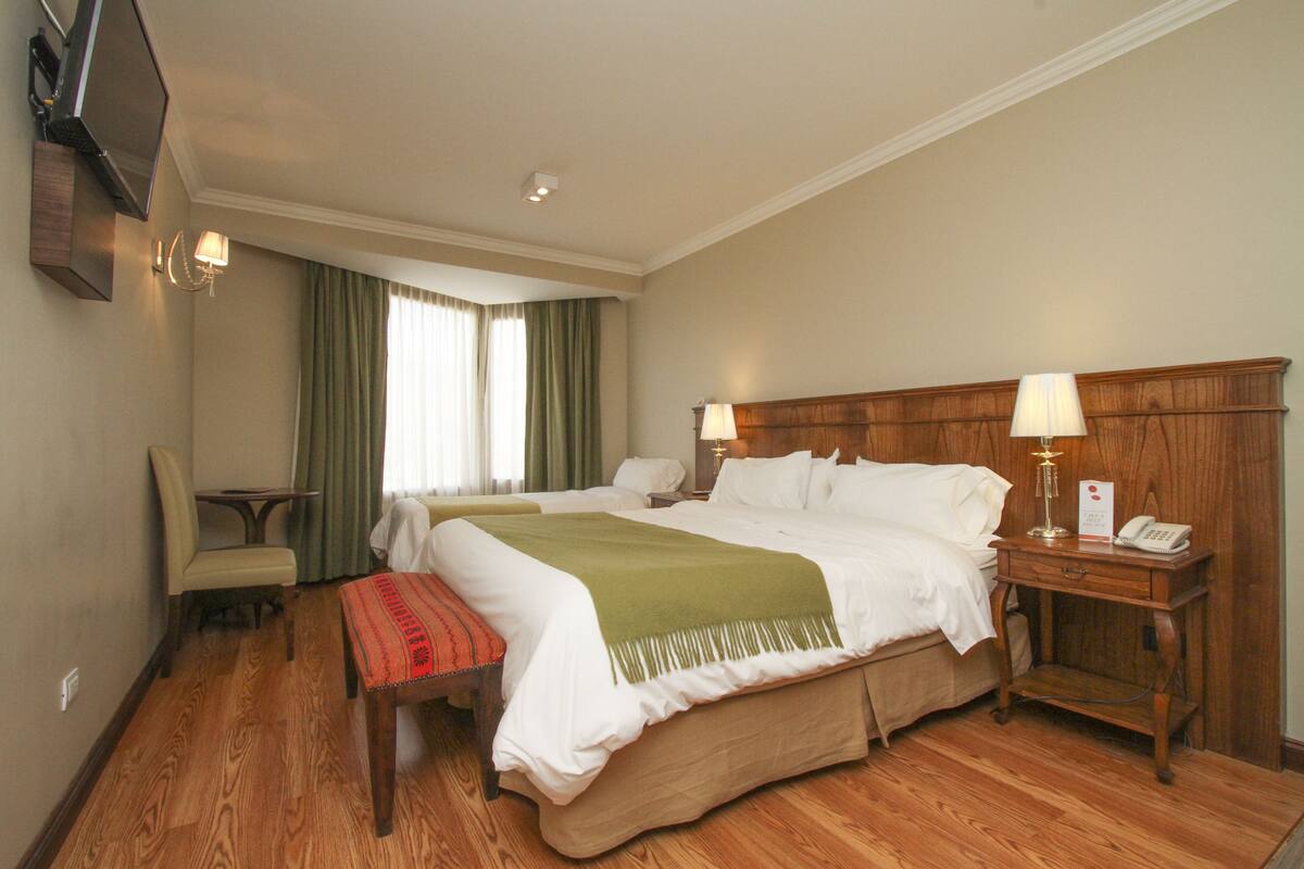 Une chambre d’hôtel avec un grand lit, des tables de chevet avec des lampes, une chaise et un bureau.