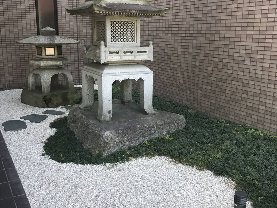A traditional Japanese garden with a multi-tiered stone lantern, a smaller lantern, and a stone pagoda.