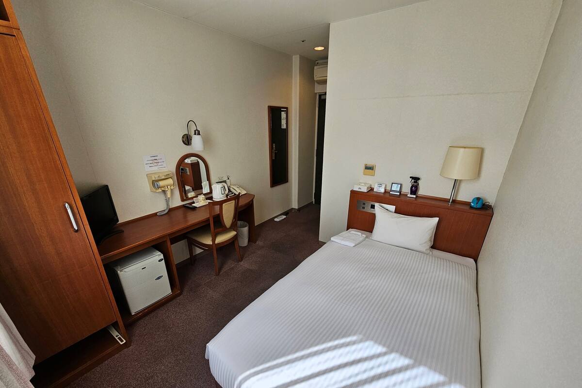 Une chambre d’hôtel équipée d’un lit, d’un bureau avec une chaise, d’un miroir, d’un téléphone et d’un petit radiateur.