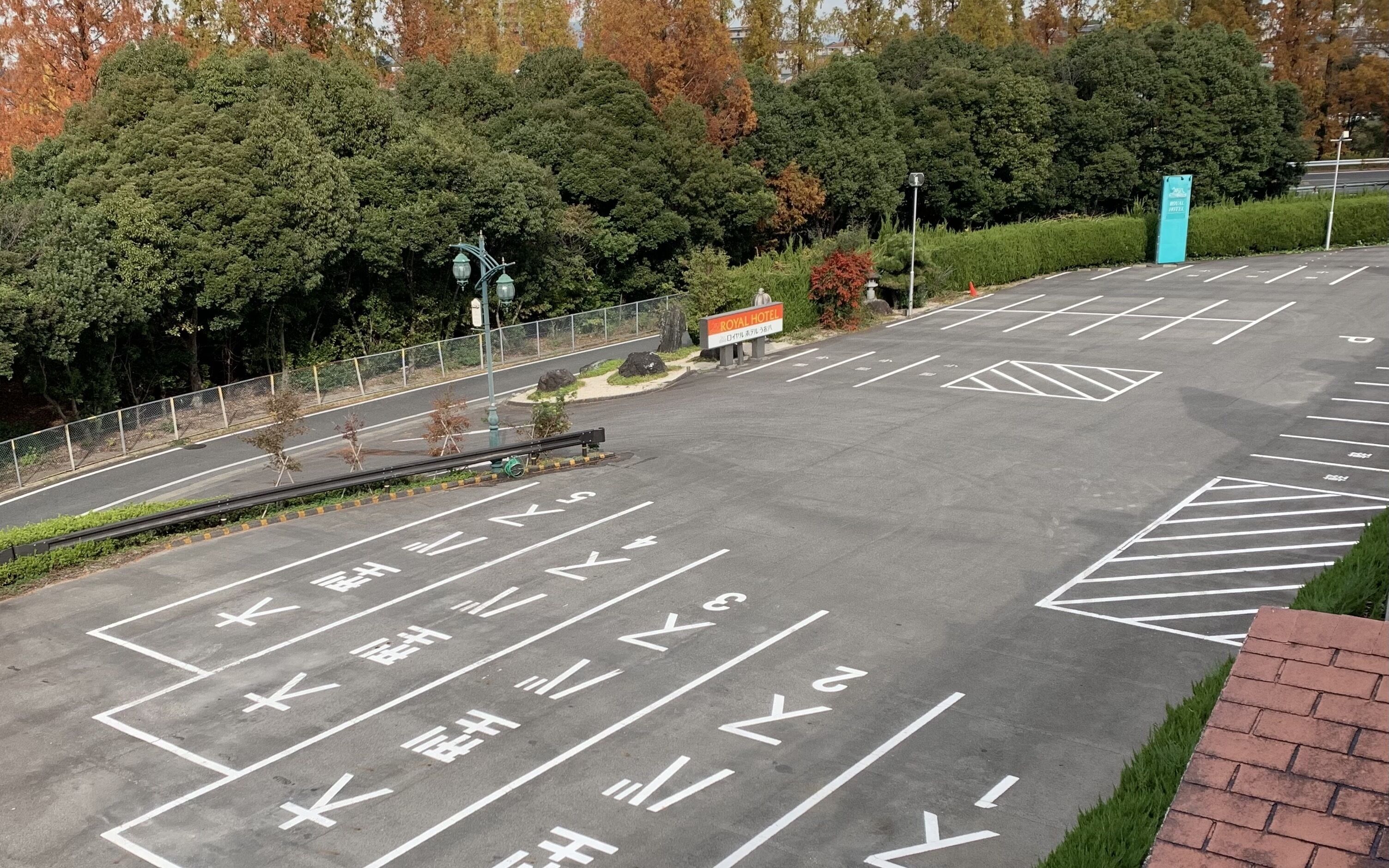 A parking lot with marked spaces and directional arrows, surrounded by trees and a fence.
