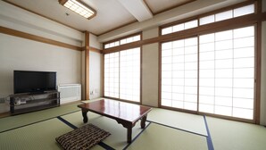 A traditional Japanese room with tatami flooring, a low wooden table, a television, and large shoji screens. - Royal Hotel Uohachi (Toyota)