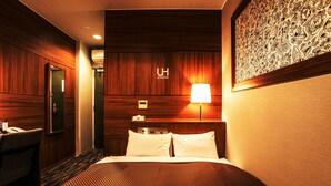 A hotel room with a bed, a desk, a chair, a wall-mounted air conditioner, and a wall with a patterned design. - Royal Hotel Uohachi (Toyota)