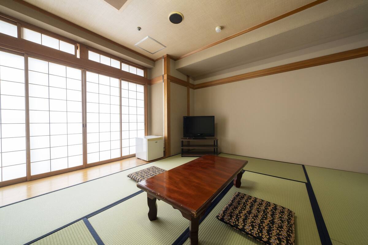 Une pièce de style japonais traditionnel, avec un sol recouvert de tatamis, une basse table en bois, un téléviseur et des portes coulissantes.