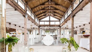 A spacious venue with a high wooden ceiling and large windows, featuring a central white sign with "BLUE BAY" and a potted plant. - Blue Bay Lodge (Saldanha)