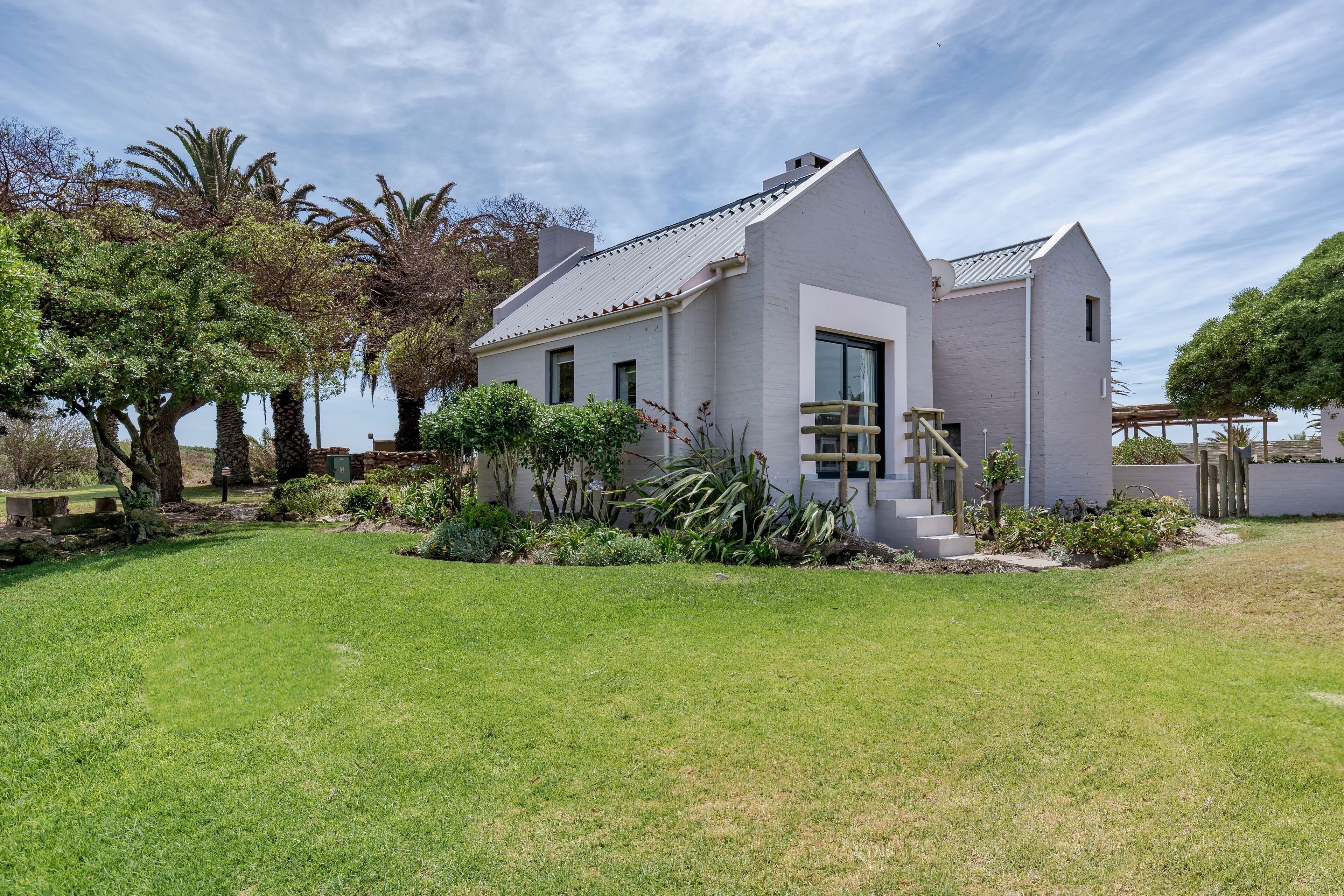 A modern two-story house with a sloped roof, surrounded by a well-maintained lawn and various plants.