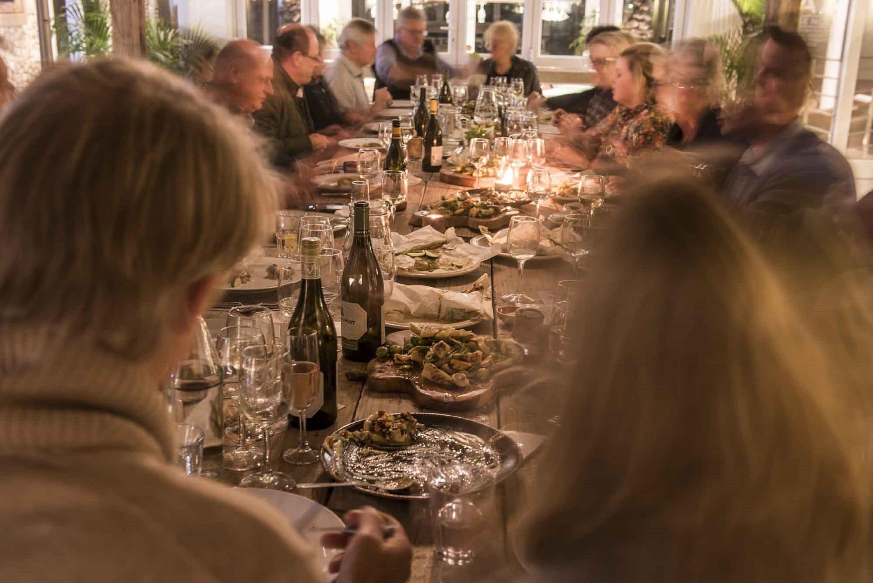 Un grupo de personas sentadas alrededor de una mesa con varios platos y botellas de vino.