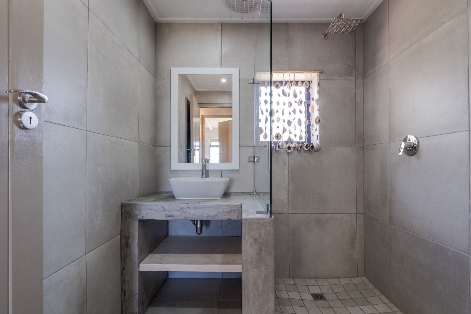 A modern bathroom with a glass-enclosed shower, a marble sink, and a view of the adjacent room.