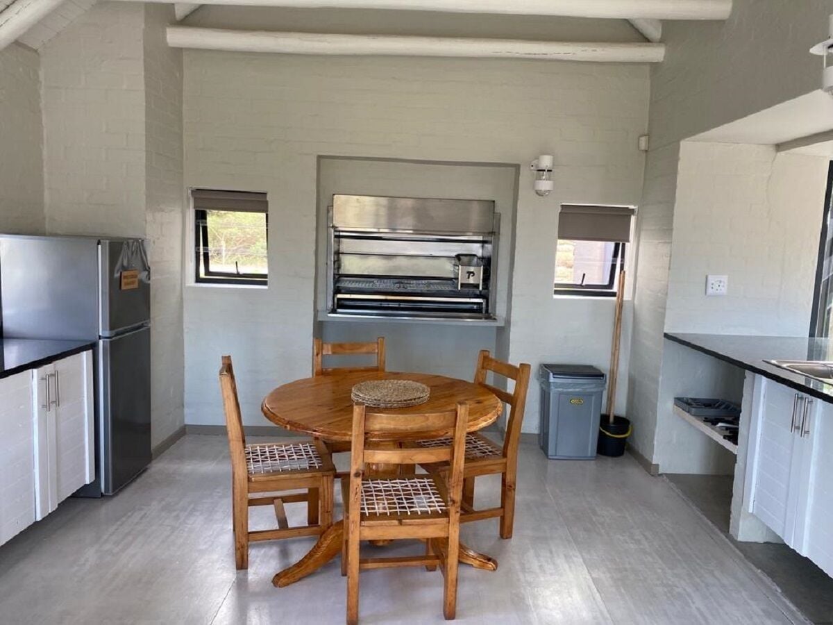 Een kleine keuken met een ronde houten tafel, vier stoelen, een inbouwoven en een koelkast.