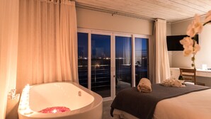 A hotel room with a bathtub, a bed, a desk, and a view of the city at night. - Blue Bay Lodge (Saldanha)