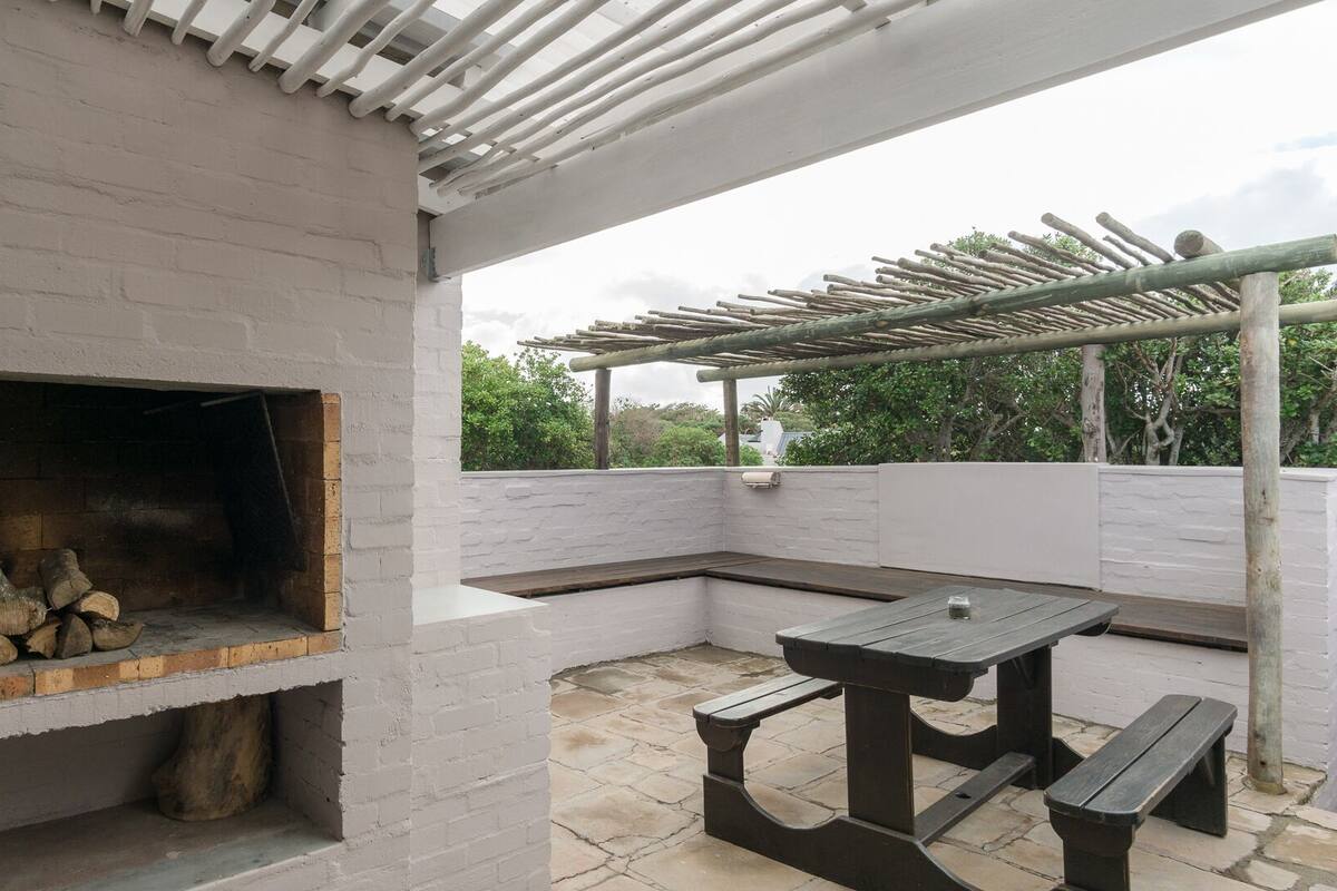 A patio with a brick fireplace, a pergola, and a wooden table and bench.