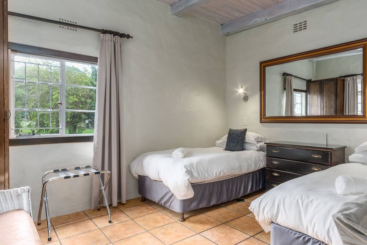 A bedroom with two beds, a dresser, a mirror, and a window with curtains.