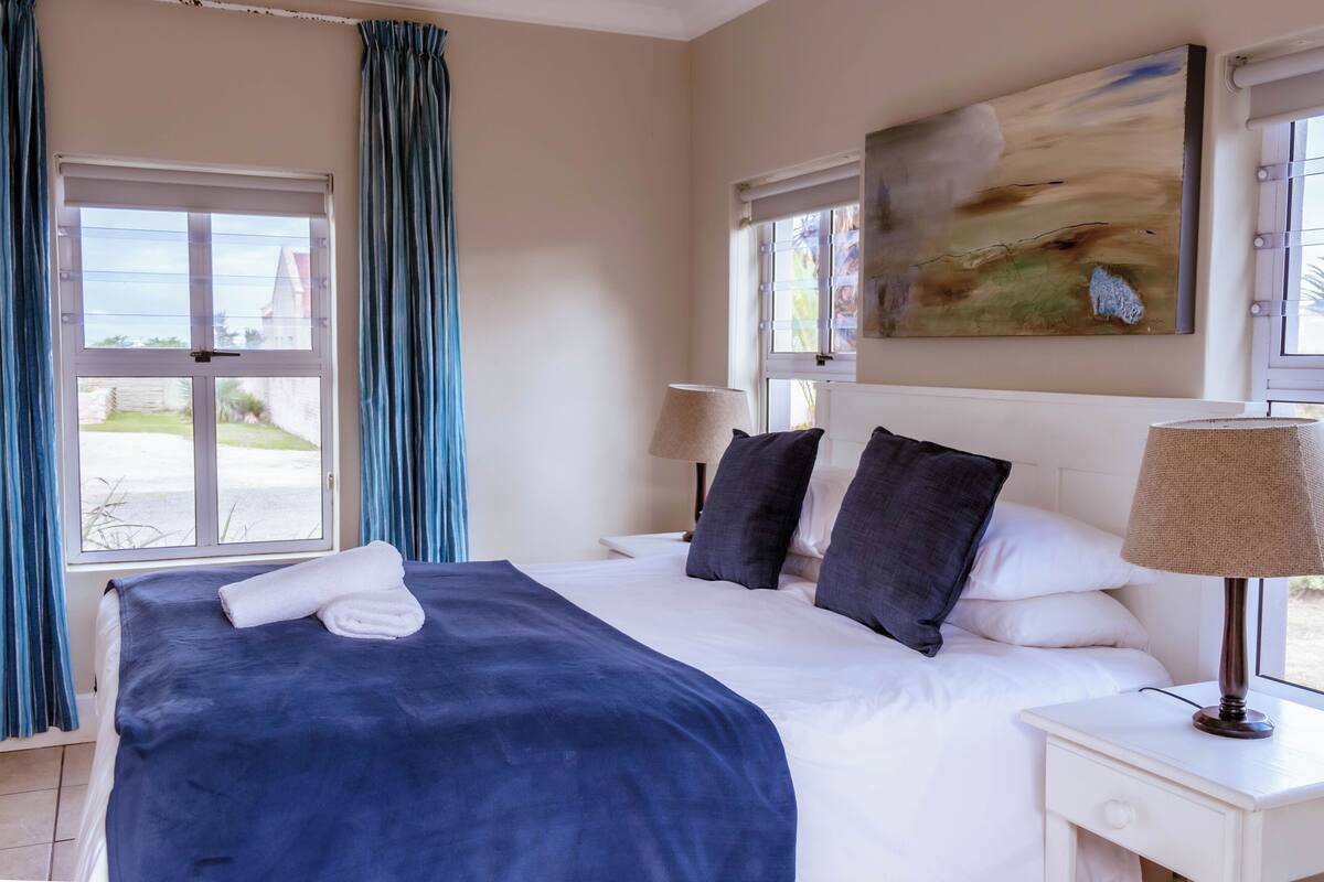 A hotel room with a bed, a nightstand, a lamp, and a painting on the wall.
