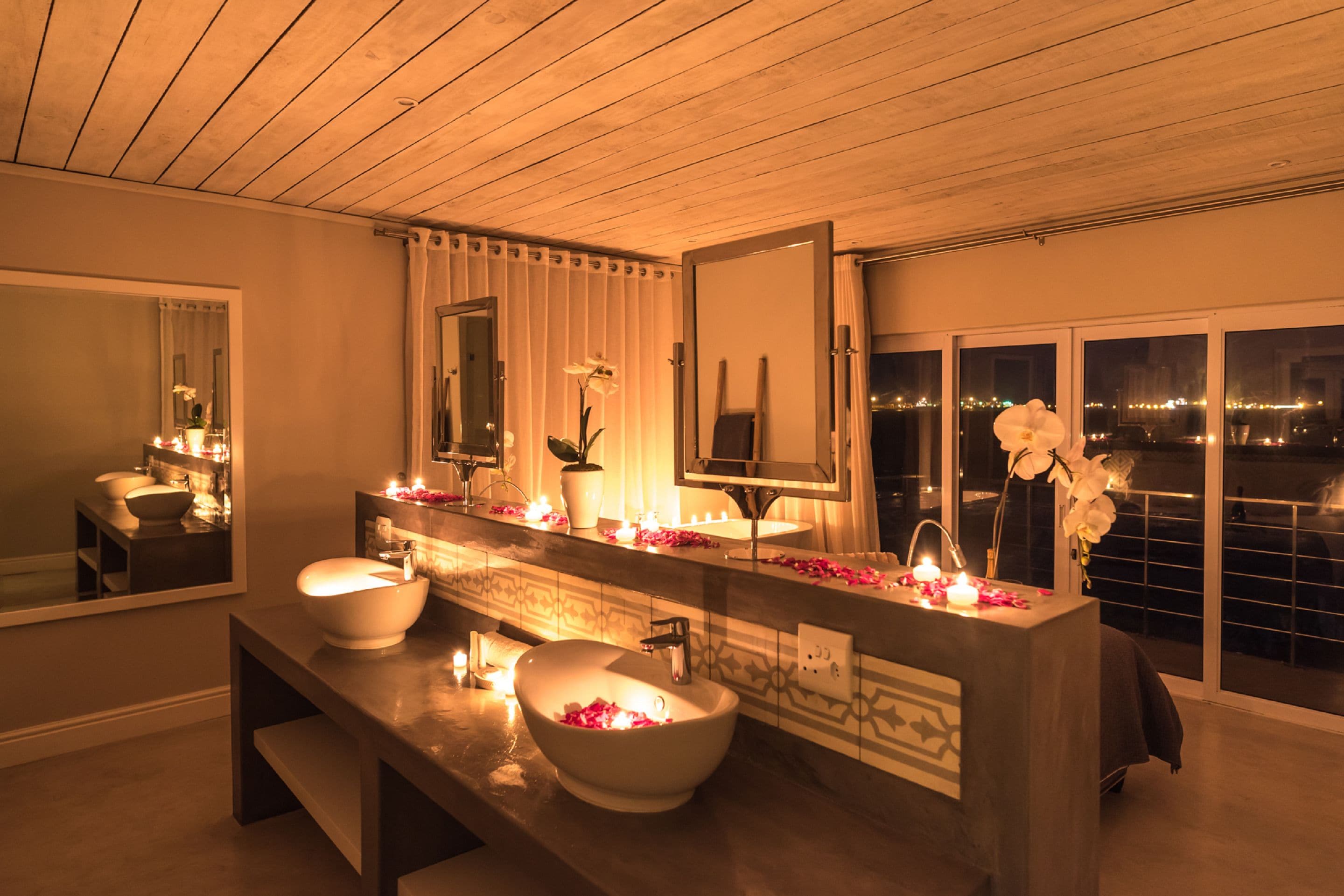 A modern bathroom with a large mirror, two sinks, and a bench.