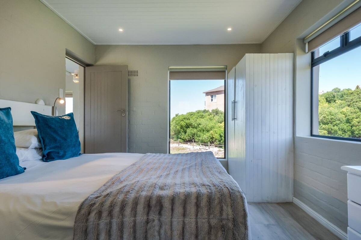 A bedroom with a large bed, a view of greenery outside, and a sliding door leading to an outdoor area.