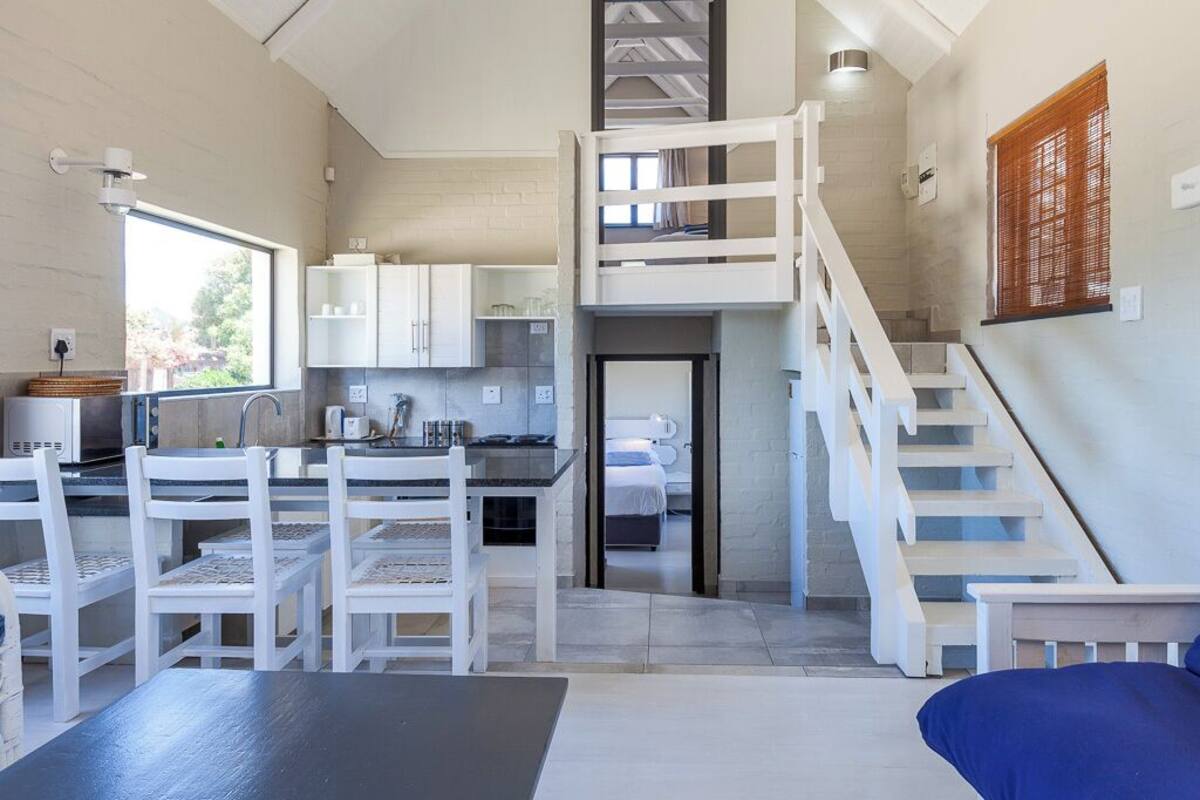 A modern interior with a kitchen, dining area, and a staircase leading to a loft bedroom.