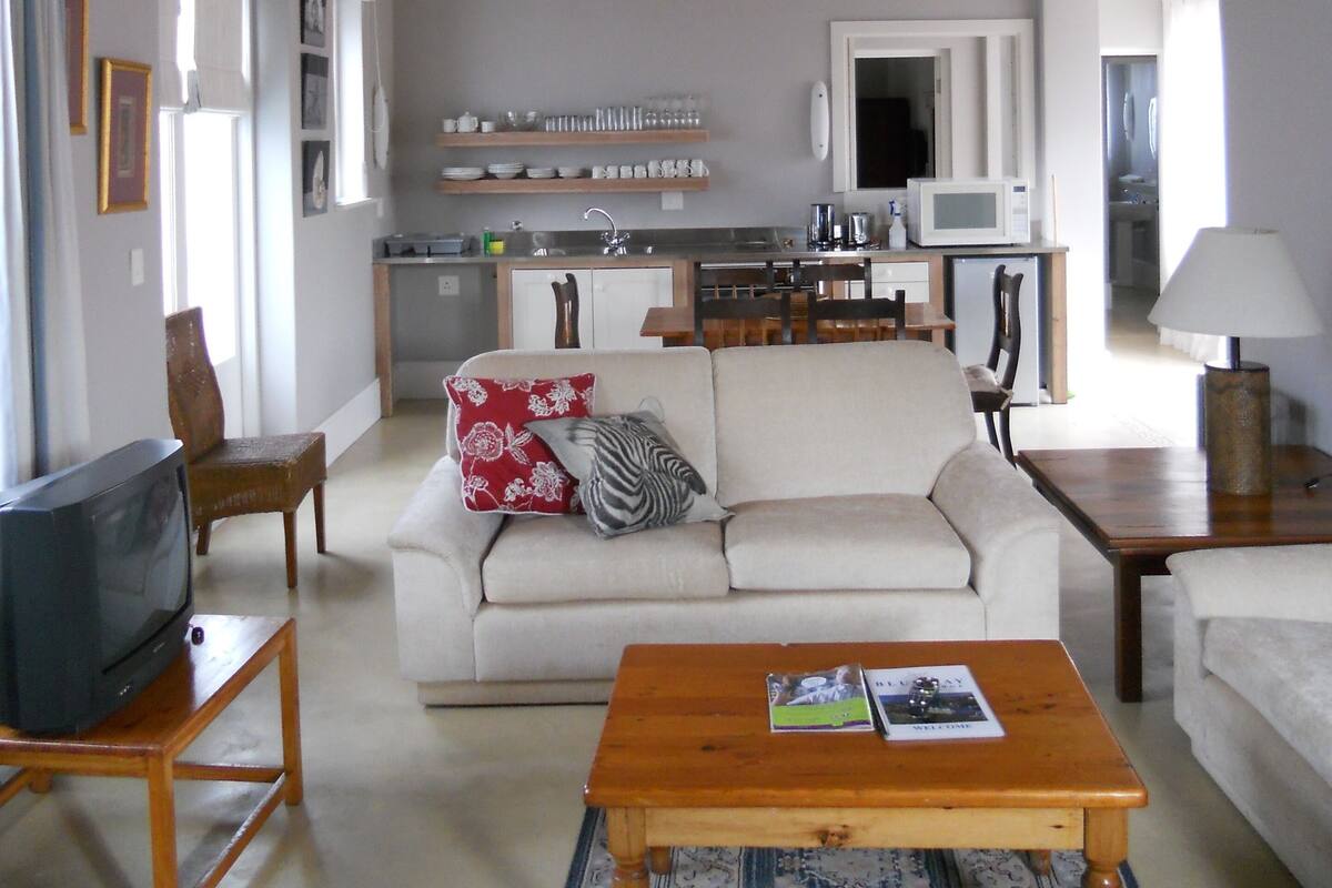 A spacious living room with a high wooden ceiling, a white sofa, a wooden coffee table, and a kitchen in the background.