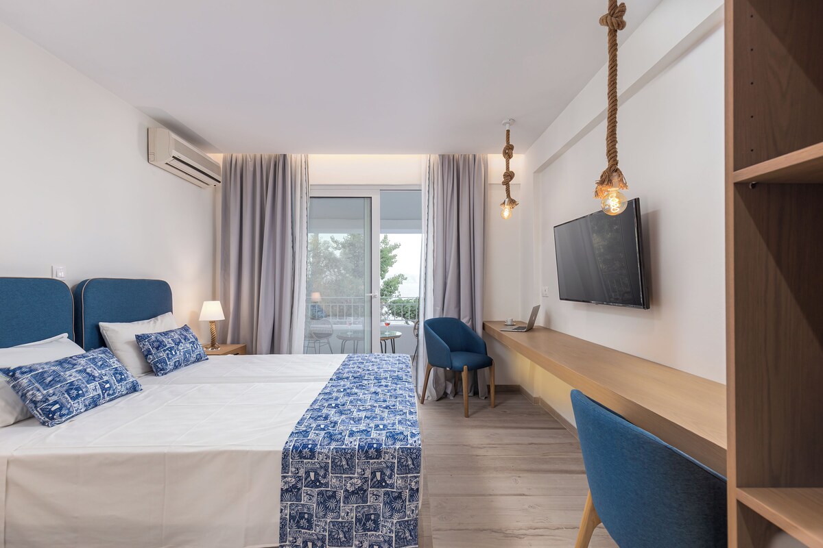 Habitación de hotel con cama, escritorio, laptop, televisión y vistas al exterior.