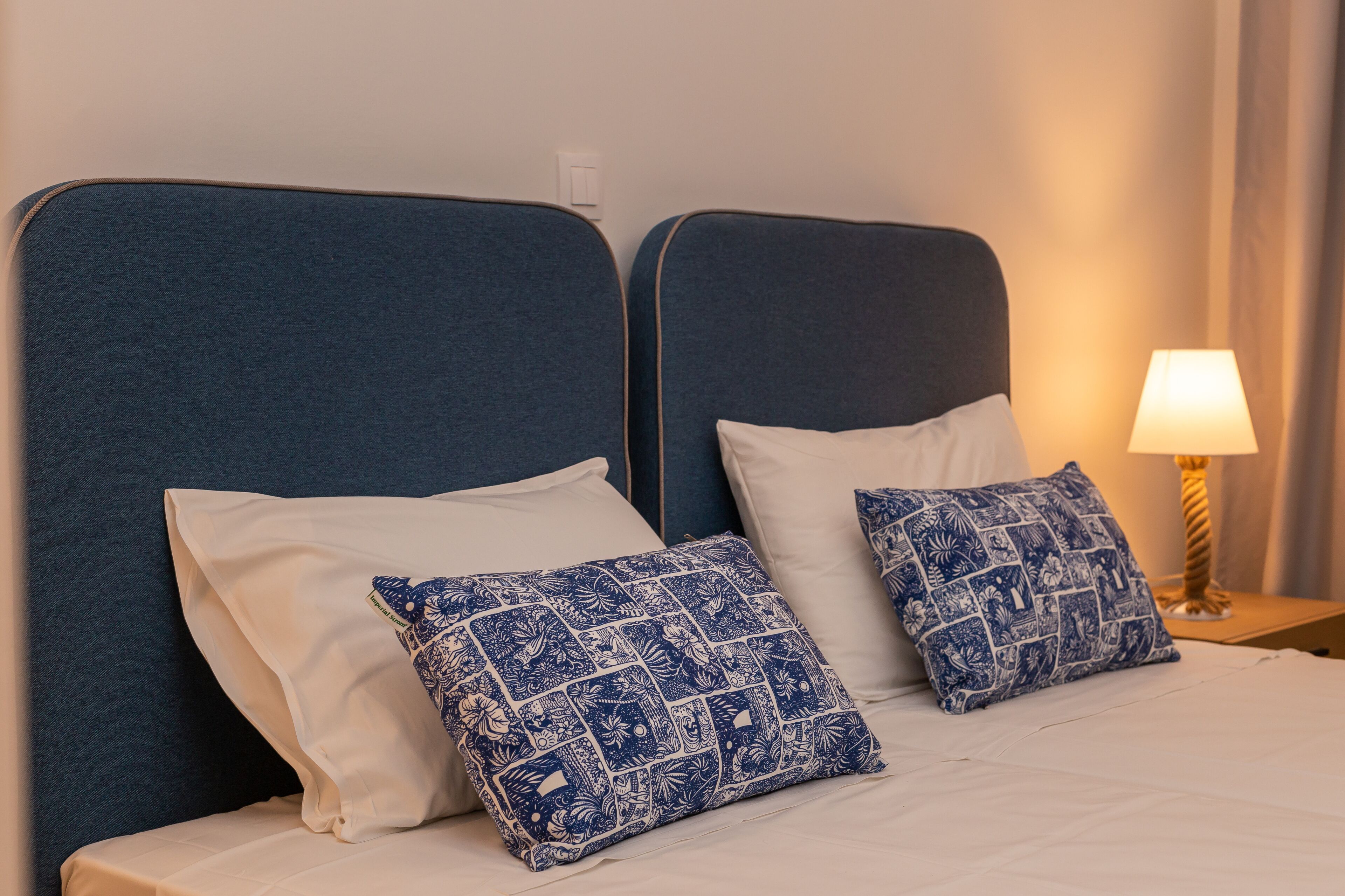 A double bed with two pillows, one white and one with a blue floral pattern, against a blue headboard.
