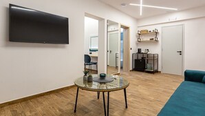 Een moderne woonkamer met een flatscreen televisie, een ronde glazen tafel, een blauwgroene bank en een houten vloer.