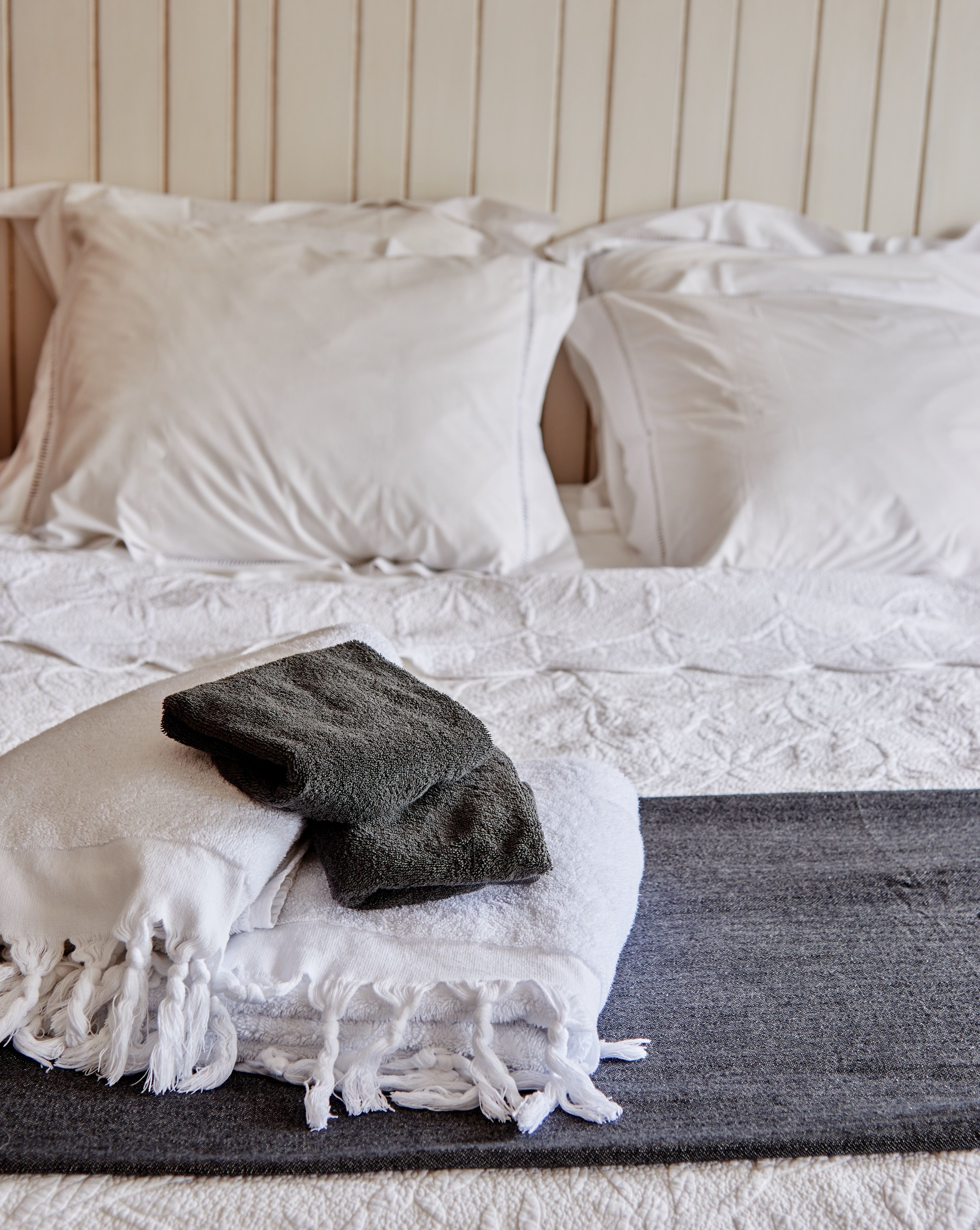 A neatly made bed with white linens and a dark gray towel placed on a yoga mat.