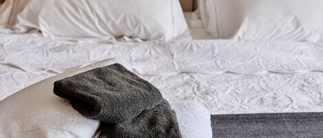 Un lit bien fait, avec du linge de lit blanc et une serviette gris foncé posée sur un tapis de yoga.