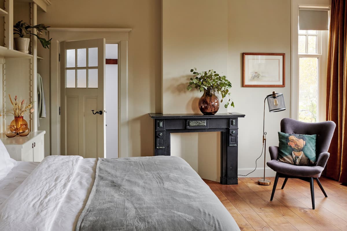A bedroom with a bed, a dresser, a desk with a vase, a chair, and a window with curtains.